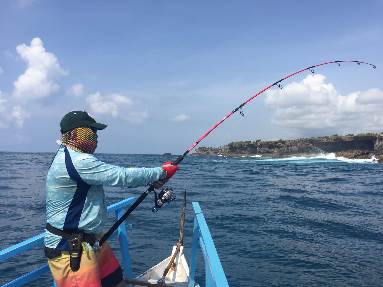 Angler fishing from a boat beside a rocky island in Malaysian waters